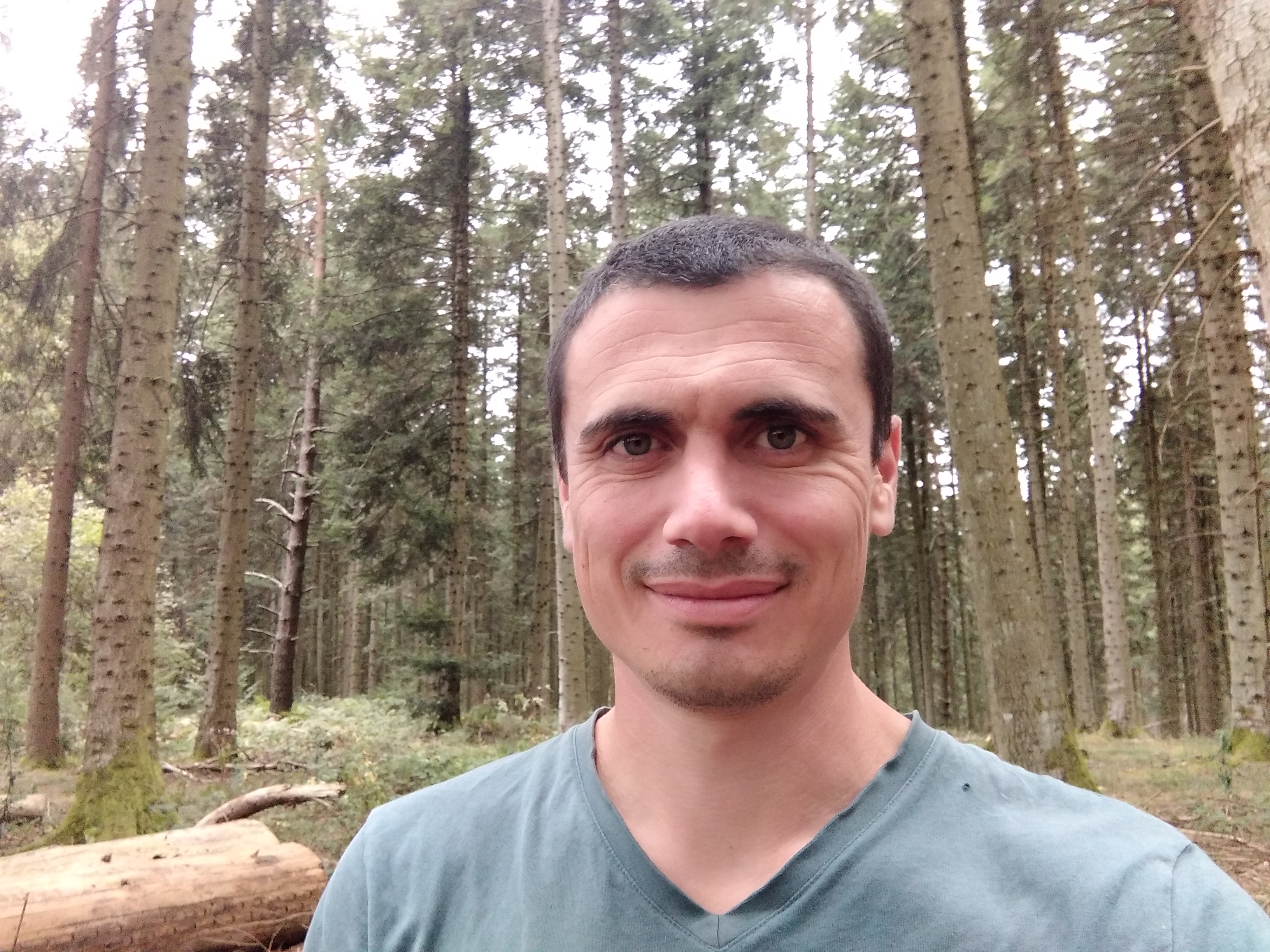 Nicolas Renvoisé smiling in a green t-shirt surrounded by forest trees